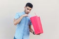 Unboxing and looking inside of bag. Portrait of handsome young bearded man in blue shirt standing, holding red shopping bag, Royalty Free Stock Photo