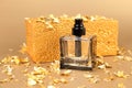 Unbranded black square perfume spray bottle, pieces of gold paper and golden rectangular shape on golden background. Front view,