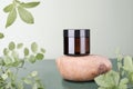 unbranded brown glass jar on natiral stone podium and green branches and leaves. cosmetic product, collagen peptides