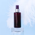 Unbranded brown sunscreen spray bottle on glass podium and large white ostrich feather on blue background. Blank label bottle for Royalty Free Stock Photo