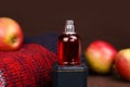 Unbranded Perfume spray red bottle on elegant navy blue box podium, red apples and Christmas or autumn red knitted sweater on