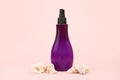 Unbranded purple plastic spray bottle and many different sea shells on pink background. Cosmetic packaging mockup with copy space