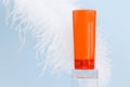 Unbranded red orange shampoo and conditioner bottle for branding and label on glass podium and large white ostrich feather on blue