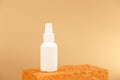 Unbranded white cosmetics spray bottle on golden podium on gold background. Front view, mockup. Cosmetic bottle container for