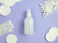 Unbranded white plastic bottle of disinfectant, cotton pads and sticks on purple background. Natural organic spa cosmetics and