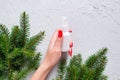 Unbranded white plastic spray bottle, female hand with red nails and branches of christmas fir tree on gray table. Natural organic Royalty Free Stock Photo