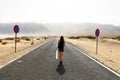 Uncertain future. Young alone woman advances with an uncertain step in empty asphalt desert road. Apocalypse concept