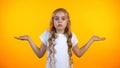 Uncertain preteen girl lifting hands in dismay isolated on yellow background
