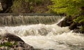 Unclean polluted river water forms a small waterfall in a forest park