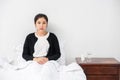 An uncomfortable woman sits on the bed and has medicine on the table