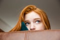 Unconfident shy redhead girl peeping from sofa