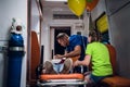 Unconscious mother lying on a stretcher in an ambulance car, a paramedic providing her first aid