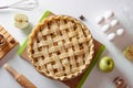 Uncooked apple pie into a baking dish ready for cooking on a white table surrounded by ingredients