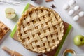 Uncooked apple pie into a baking dish ready for cooking on a white table surrounded by ingredients