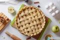 Uncooked apple pie into a baking dish ready for cooking on a white table surrounded by ingredients