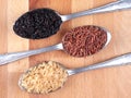 Uncooked black, red and integral rice on silver spoons, flat lay