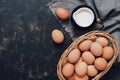 Uncooked brown eggs in a basket and milk in a jug on a dark rustic background. Top view, copy space.