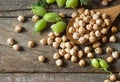 Uncooked dried chickpeas in wooden spoon with raw green chickpea pod plant on wooden table