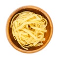 Uncooked, dried tagliatelle pasta, flat ribbons, in a wooden bowl