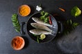 Uncooked fresh fish on a black pan along with spice condiments with use of selective focus. Royalty Free Stock Photo