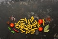 Uncooked fusilli pasta on a black stone background with spices and cherry tomatoes. Top view, copy space, flat lay Royalty Free Stock Photo