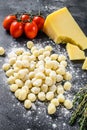 Uncooked homemade potato gnocchi with ingredients for cooking pasta. Black background. Top view