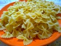 Uncooked italian pasta farfalle on an orange plate. Bow-tie pasta or butterfly macaroni. Strichetti or farfalloni. Home cooking. F