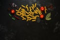 Uncooked pasta fusilli on black stone background with spices and cherry tomatoes. Top view, copy space, flat lay Royalty Free Stock Photo