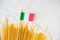 Uncooked pasta spaghetti macaroni and small italian flag on white floured background