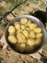 Peeled potatoes with curved funny faces are stacked in a pan with water; cooking outdoors