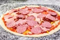 Uncooked pizza with sliced salami, ham and sausages. Royalty Free Stock Photo