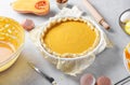 Uncooked pumpkin pie into a baking dish ready for cooking on a gray kitchen table surrounded by ingredients, close up Royalty Free Stock Photo