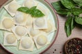 Uncooked ravioli, basil and peppercorns on wooden table, flat lay