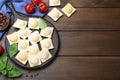 Uncooked ravioli, basil and tomato on wooden table, flat lay. Space for text