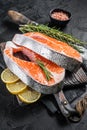 Uncooked Raw Salmon Fish Steaks on butcher board with herbs. Black background. Top view Royalty Free Stock Photo