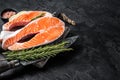 Uncooked Raw Salmon Fish Steaks on butcher board with herbs. Black background. Top view. Copy space Royalty Free Stock Photo