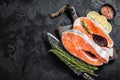 Uncooked Raw Salmon Fish Steaks on butcher board with herbs. Black background. Top view. Copy space Royalty Free Stock Photo