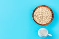 Uncooked rolled oats in bamboo bowl plant milk in white ceramic jug on light blue tabletop. Healthy vegan breakfast Royalty Free Stock Photo