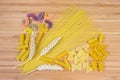 Uncooked various pasta and wheat ears on wooden surface Royalty Free Stock Photo