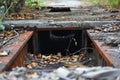 An uncovered manhole or entrance to an underground space, surrounded by worn ground and debris