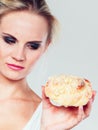 Undecided woman holds cake sweet bun in hand