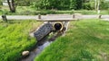 Under the asphalted road with concrete fence posts there is a concrete pipe through which a small river flows and runs further on Royalty Free Stock Photo