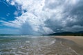 Under the blue sky and white clouds, the waves wash on the beach, and the small island in the distance