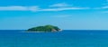 Under the blue sky and white clouds, the waves wash on the beach, and the small island in the distance