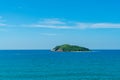 Under the blue sky and white clouds, the waves wash on the beach, and the small island in the distance