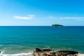 Under the blue sky and white clouds, the waves wash on the beach, and the small island in the distance