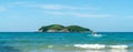 Under the blue sky and white clouds, the waves wash on the beach, and the small island in the distance