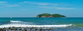 Under the blue sky and white clouds, the waves wash on the beach, and the small island in the distance