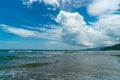 Under the blue sky and white clouds, the waves wash on the beach, and the small island in the distance