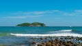 Under the blue sky and white clouds, the waves wash on the beach, and the small island in the distance